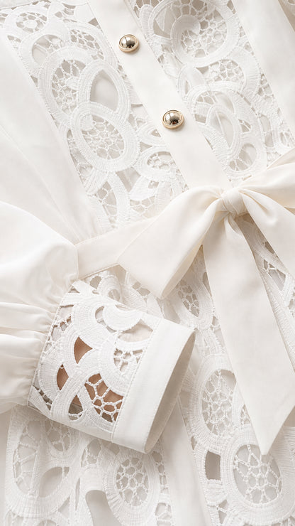 Close-up detail of white embroidered lace pattern, gold-rimmed buttons, and cuffs