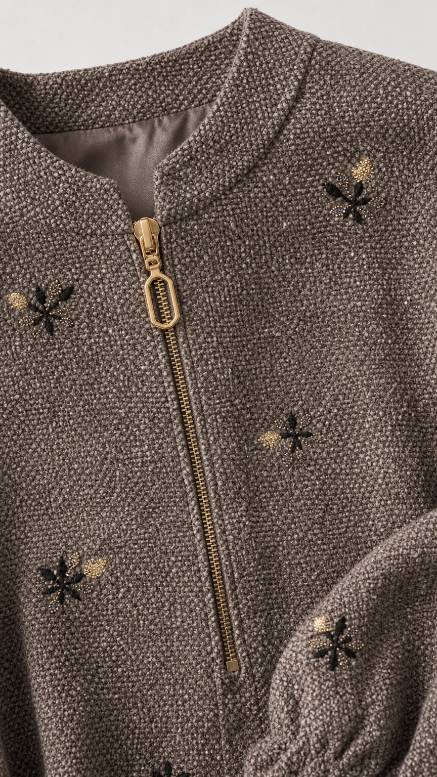 Close-up detail of taupe textured fabric, zipper, and floral embroidery