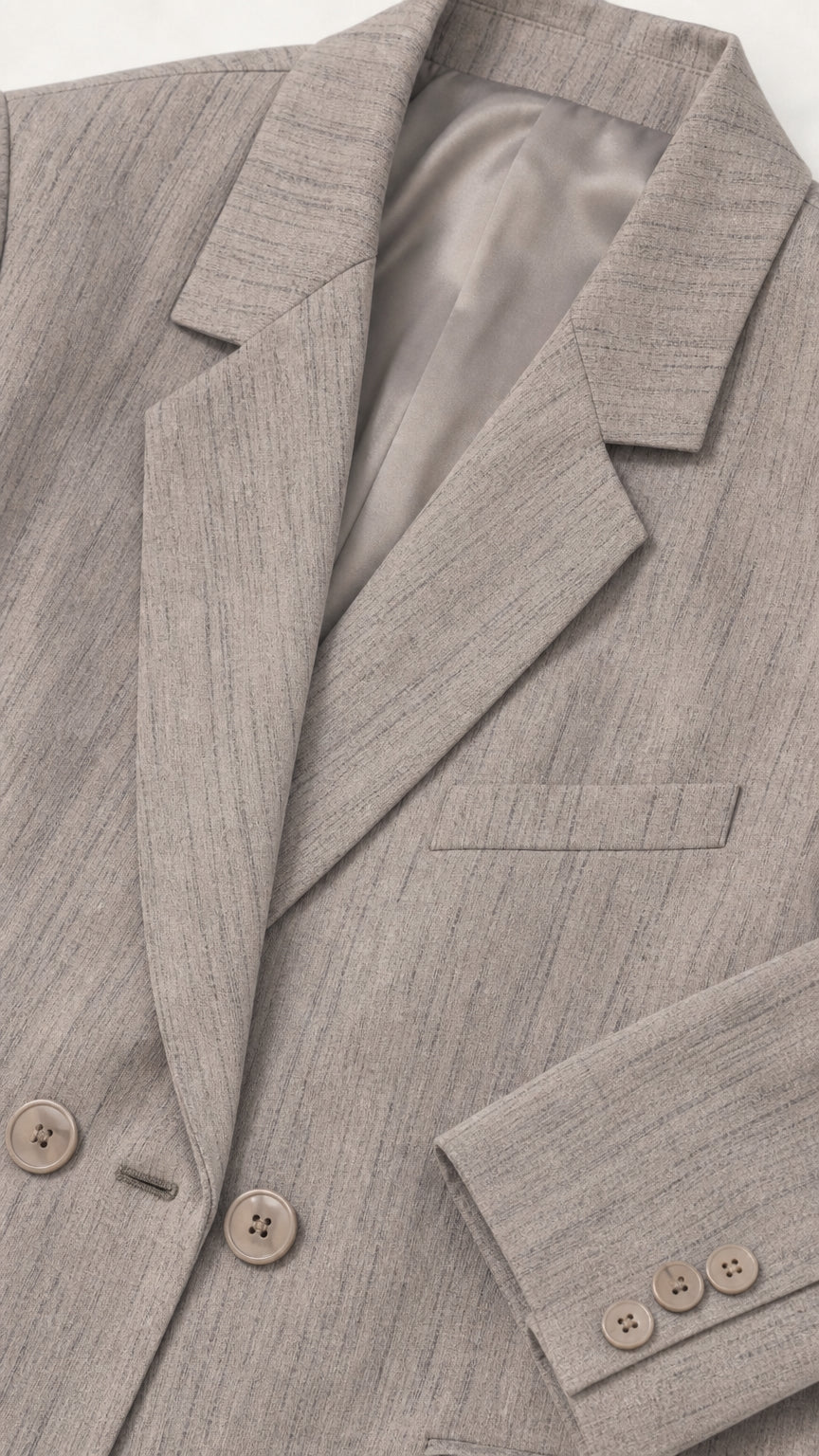 Close-up detail of textured light grey blazer lapel, buttons, lining, and sleeve cuffs
