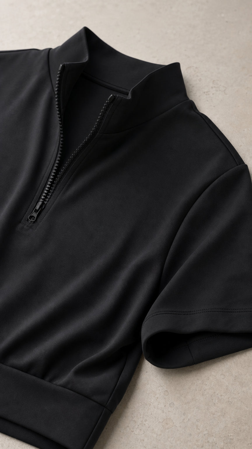 Close-up detail of black half-zip collar, zipper closure, and short sleeve