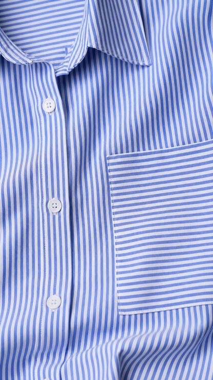 Close-up detail of blue vertical striped woven fabric, spread collar, buttons, and horizontal-striped chest pocket
