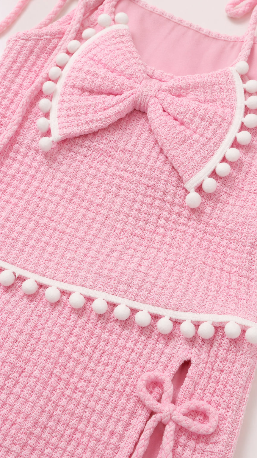 Close-up detail of pink textured knit fabric, bow accent, and white pompom trim