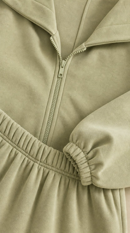 Close-up detail of zipper, elastic waistband, and cuffs on sage green tracksuit