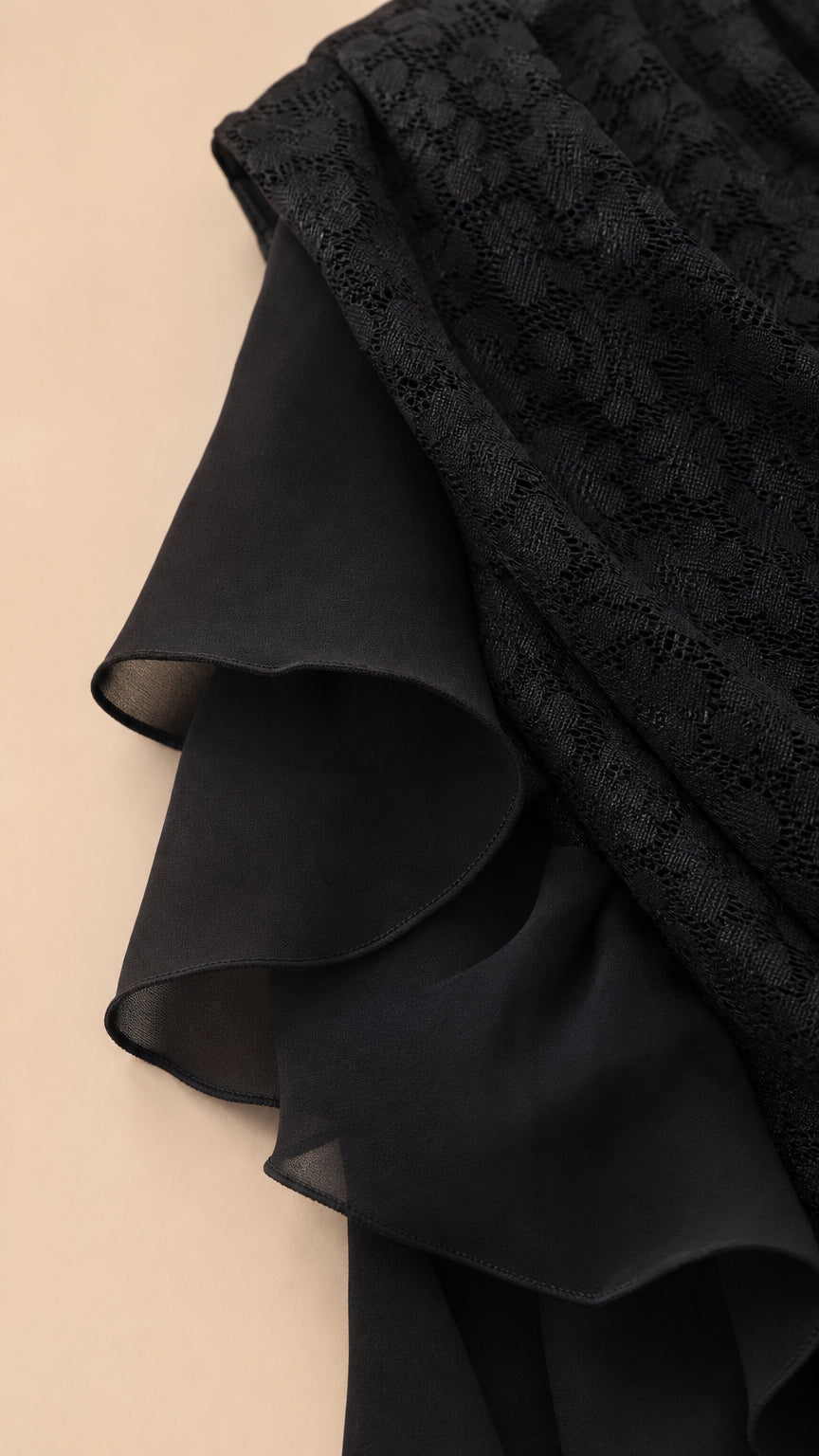 Close-up detail of black textured lace fabric and layered chiffon ruffle trim