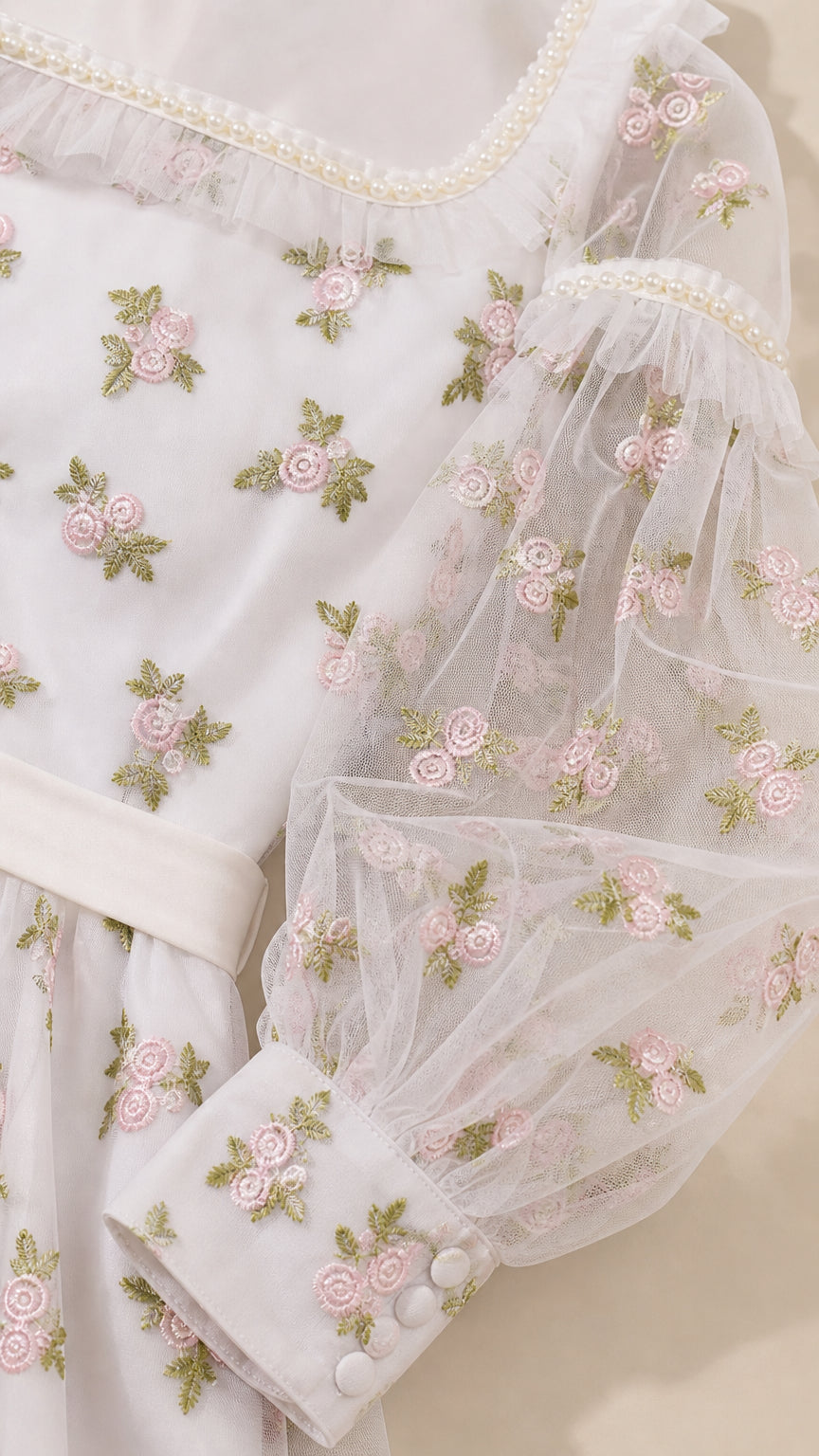 Close-up detail of floral embroidery, faux-pearl neckline, and sheer cuff sleeves