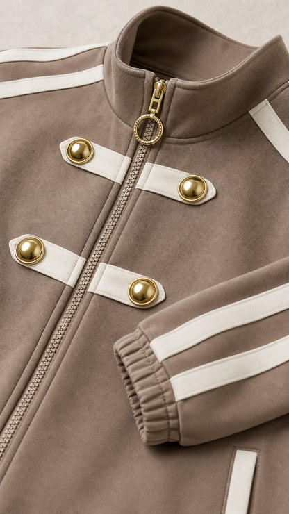 Close-up detail of taupe jacket showing gold-tone buttons, zip closure with ring pull, and ribbed cuff