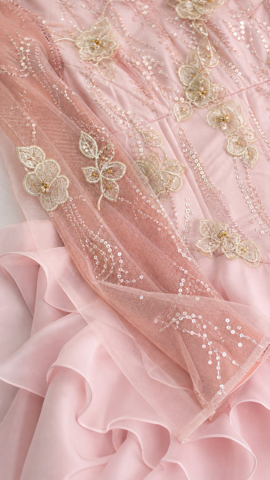 Close-up detail of sheer mesh sleeve with floral sequin embroidery and pink chiffon ruffles