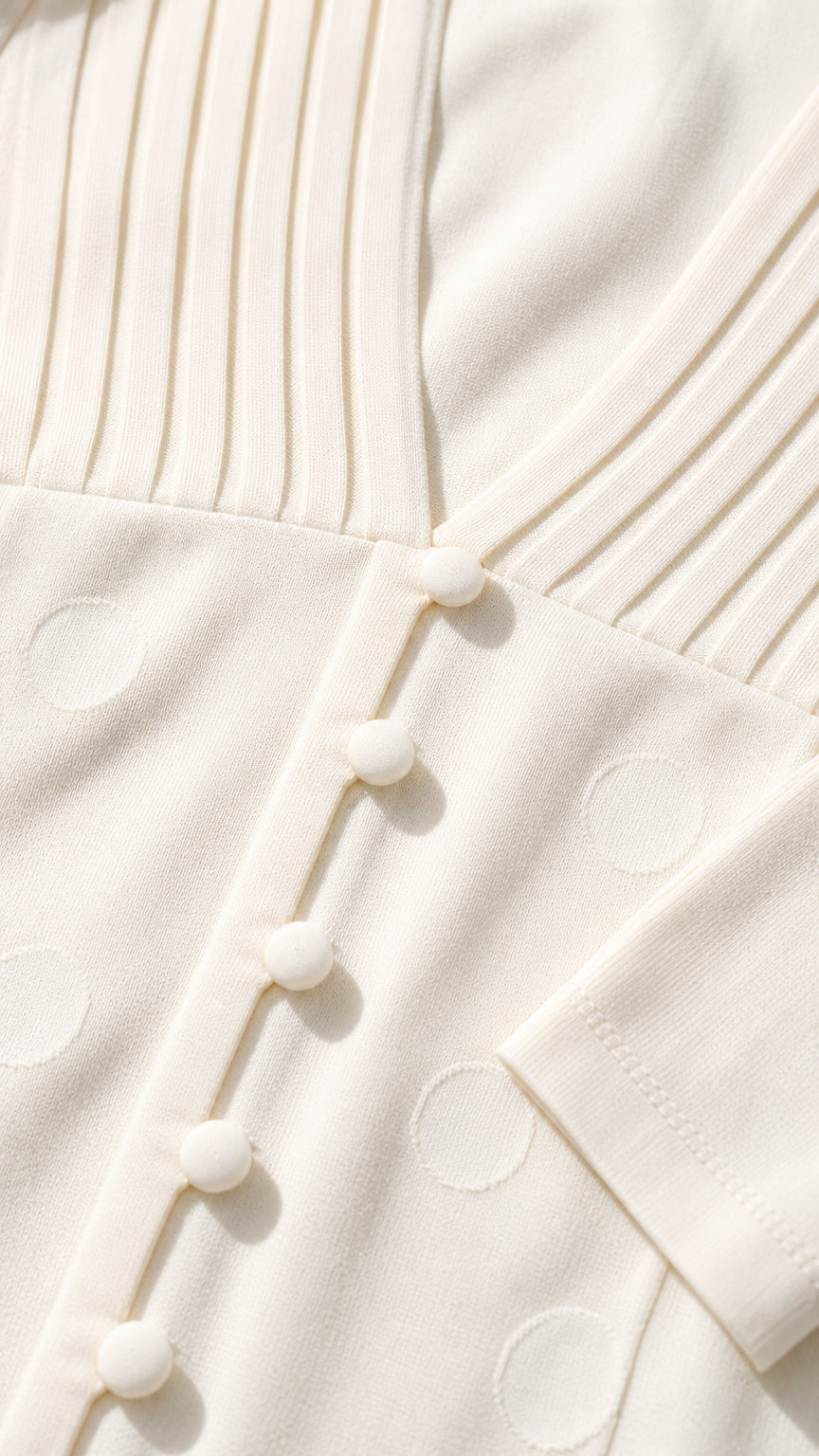 Close-up detail of cream knit fabric, ribbed neckline, and covered button closures