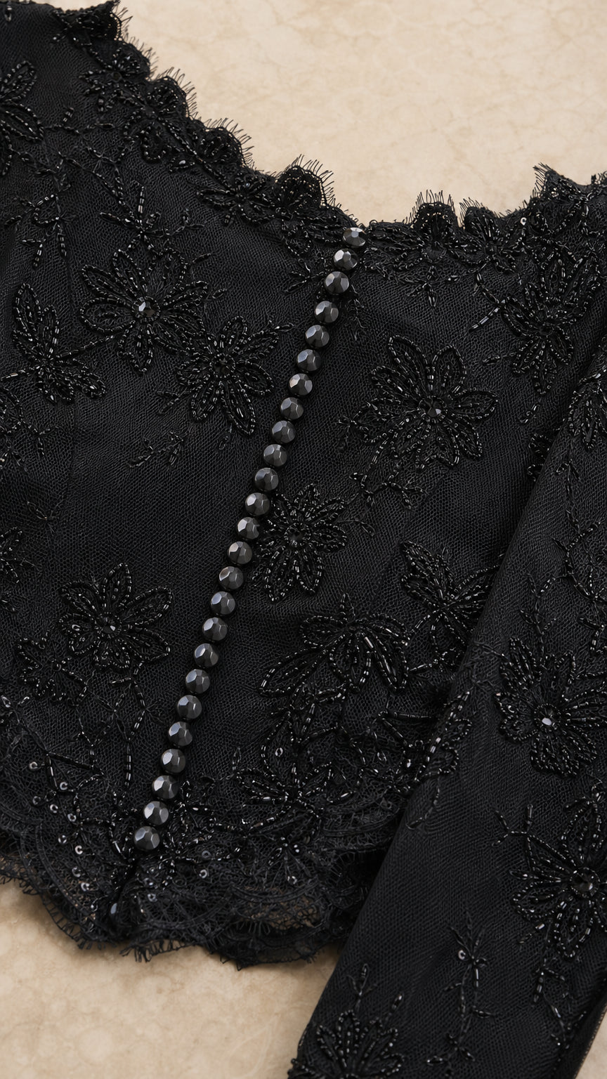 Close-up detail of black embroidered floral lace fabric and center button accents