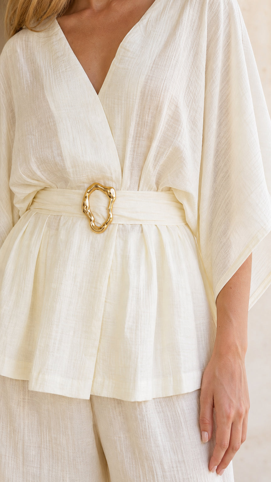 Close-up detail of textured fabric and gold-toned buckle belt on ivory top
