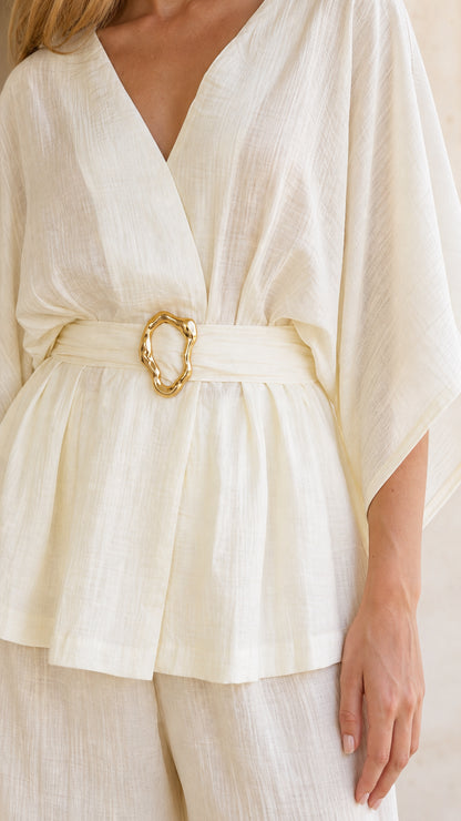 Close-up detail of textured fabric and gold-toned buckle belt on ivory top