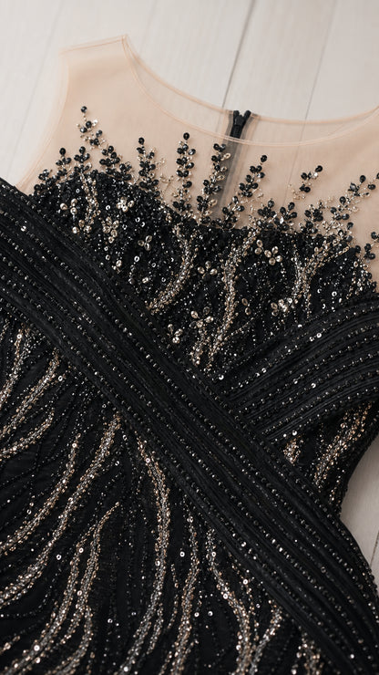 Close-up detail of sheer illusion neckline with crystal beading and pleated bust bands on black gown