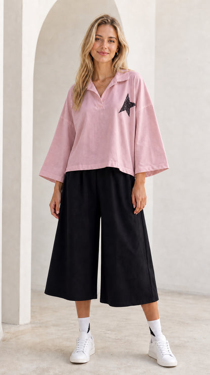 Full-length view of model wearing dusty pink star graphic polo shirt and black culottes