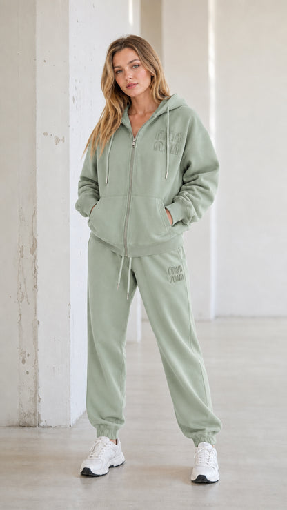 Full-body view of model wearing sage green hooded sweatshirt and jogger two-piece set