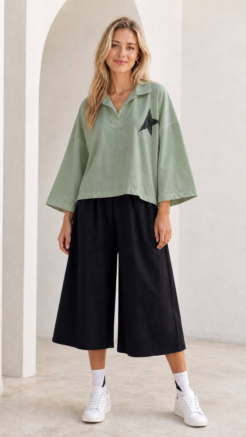 Full-length view of model wearing sage green star graphic polo top and black wide leg pants