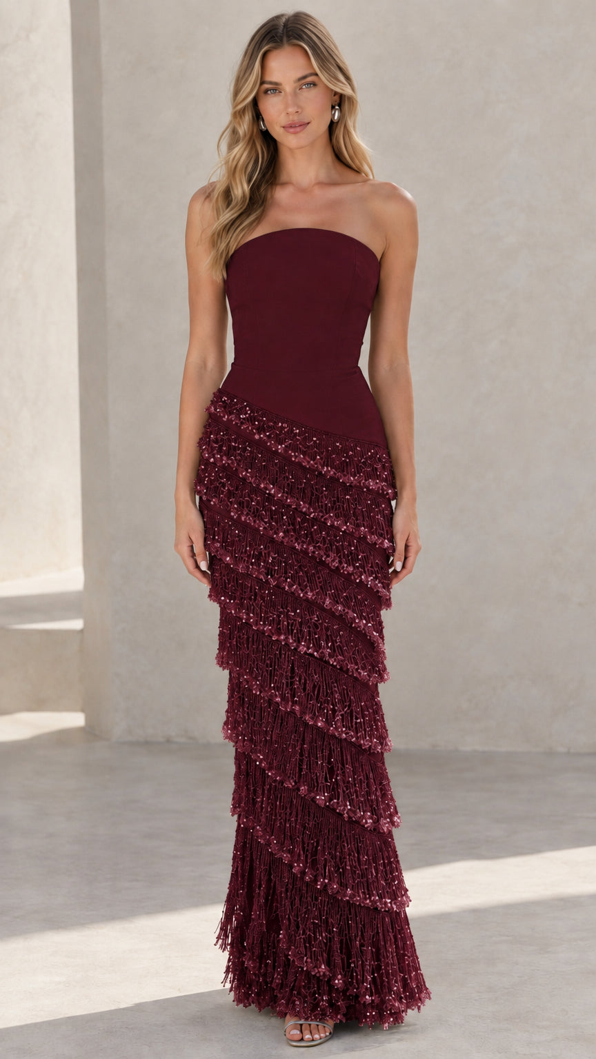 Front view of woman wearing Burgundy red strapless tiered fringe maxi gown