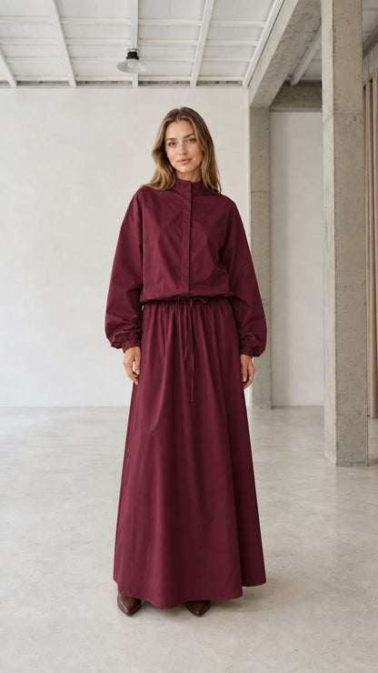 Front view of woman wearing burgundy long sleeve stand collar drawstring maxi dress