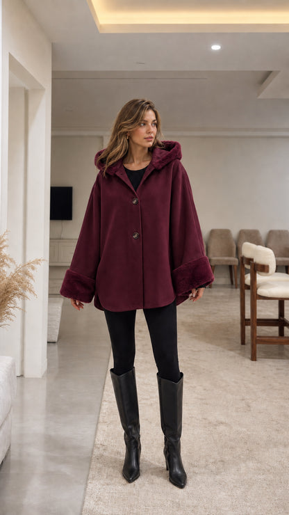 Model wearing deep burgundy hooded cape coat with faux fur trim