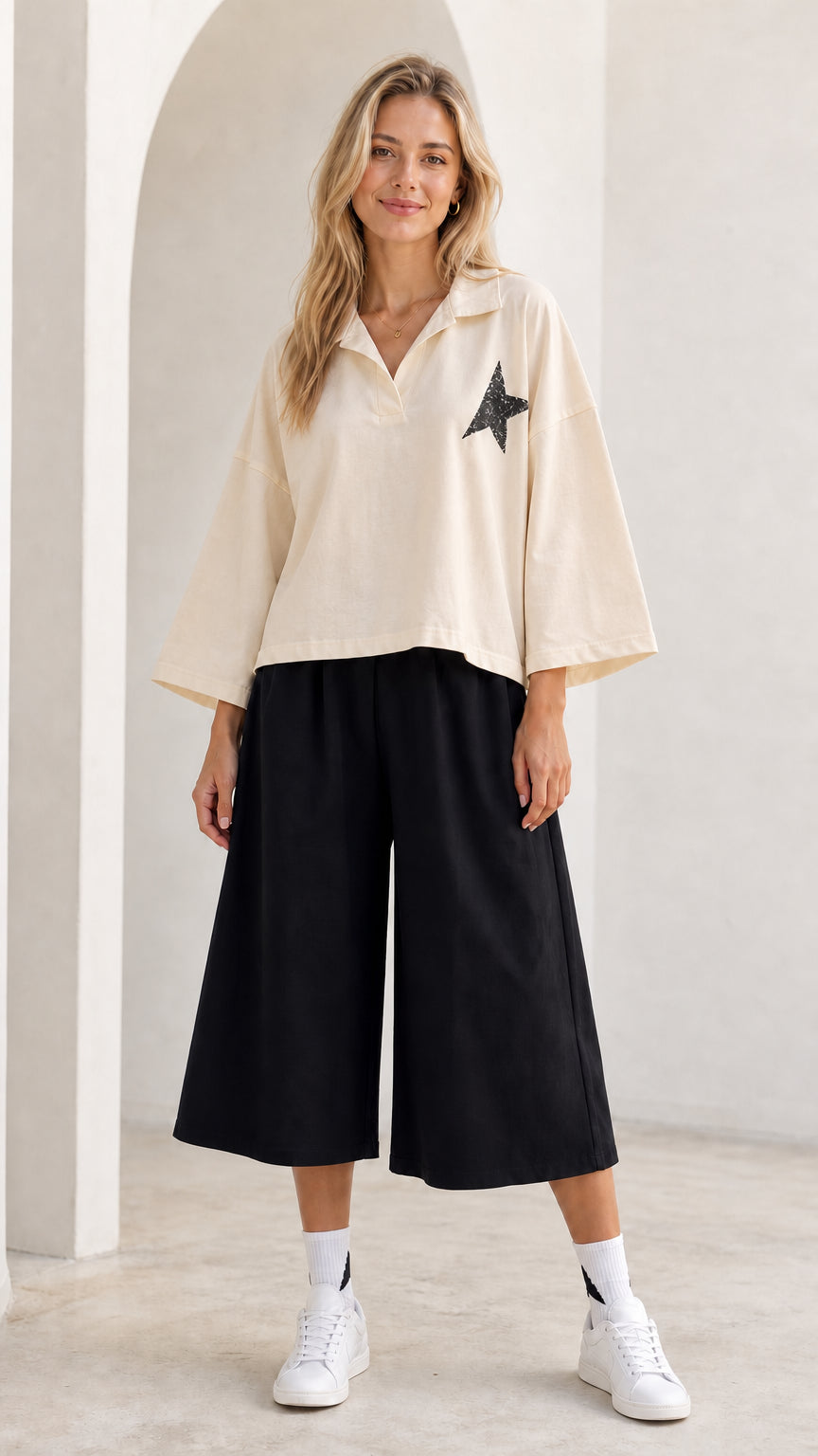 Full-length view of model wearing cream beige star graphic collared top and black culottes