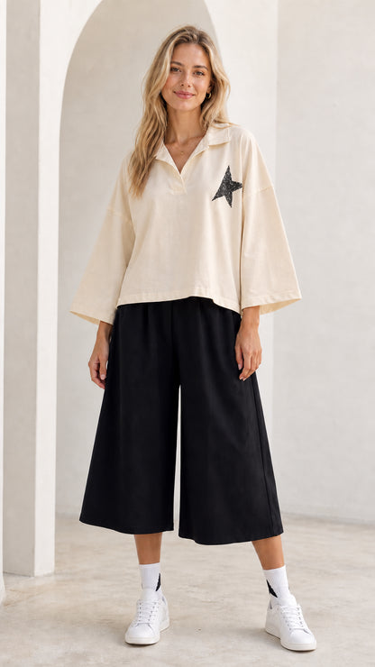 Full-length view of model wearing cream beige star graphic collared top and black culottes